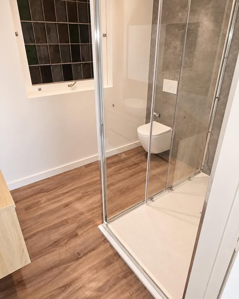 Na de renovatie: douche met glazen wand, houtlook vloer en hangtoilet