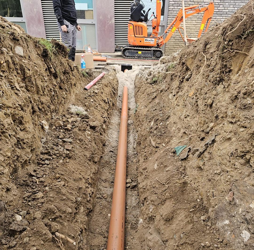 Nieuwe afvoerleiding in de uitgegraven sleuf bij het schoolgebouw